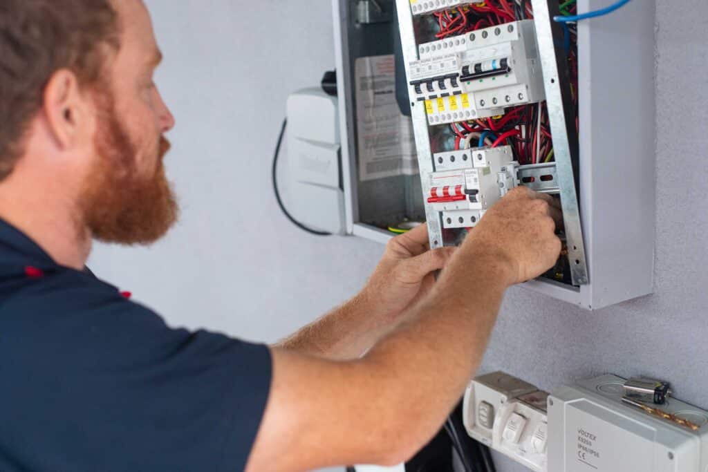 An electrician working on a circuit breaker panel, adjusting wiring inside an electrical control box.