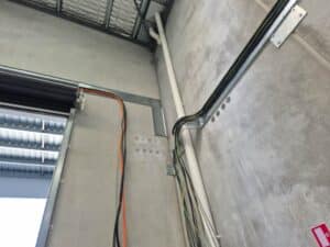 Electrical cable tray with power cables routed along a warehouse wall and ceiling.