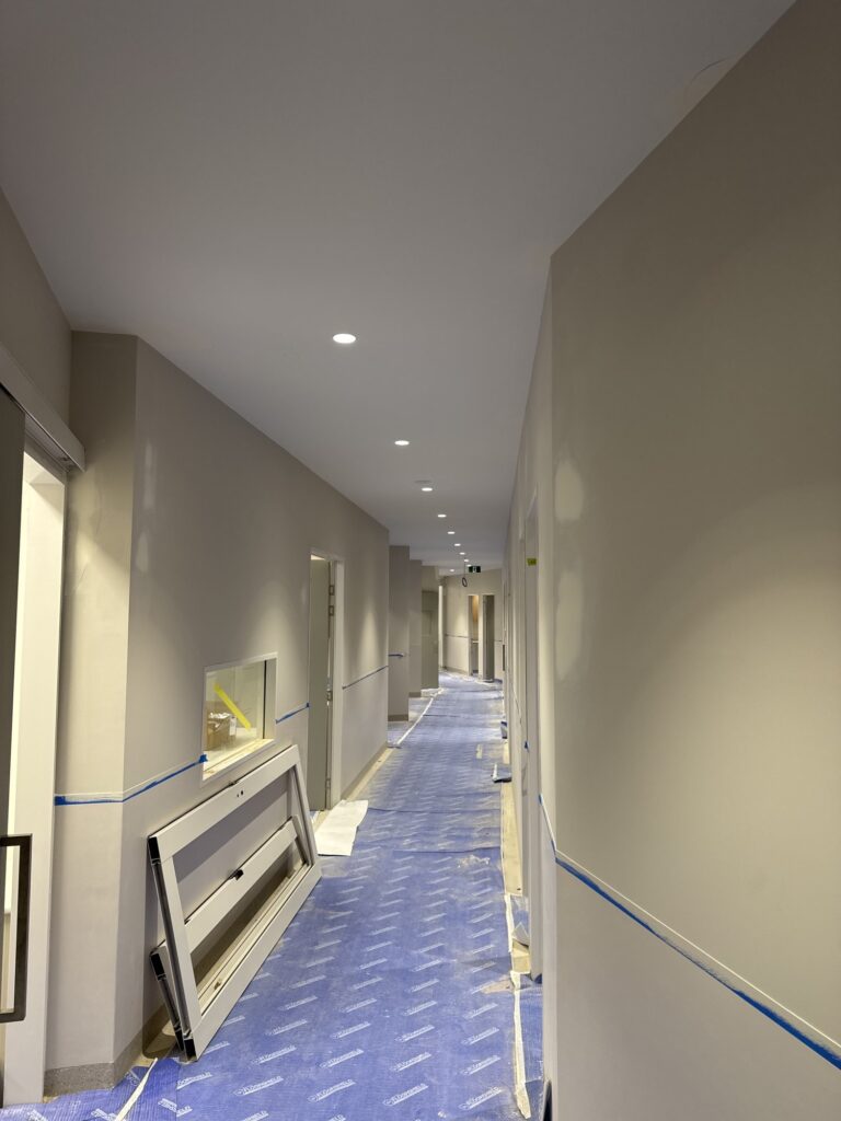 Hospital corridor under construction with recessed lighting and floor protection in place.