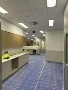 Healthcare fit-out with cabinetry, ceiling lights and protected flooring during construction.