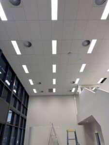 Completed commercial ceiling with LED panel lights, air diffusers and high windows.