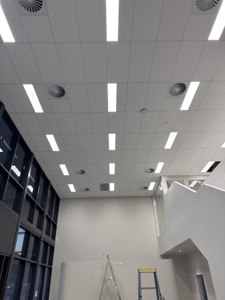 Completed commercial ceiling with LED panel lights, air diffusers and high windows.