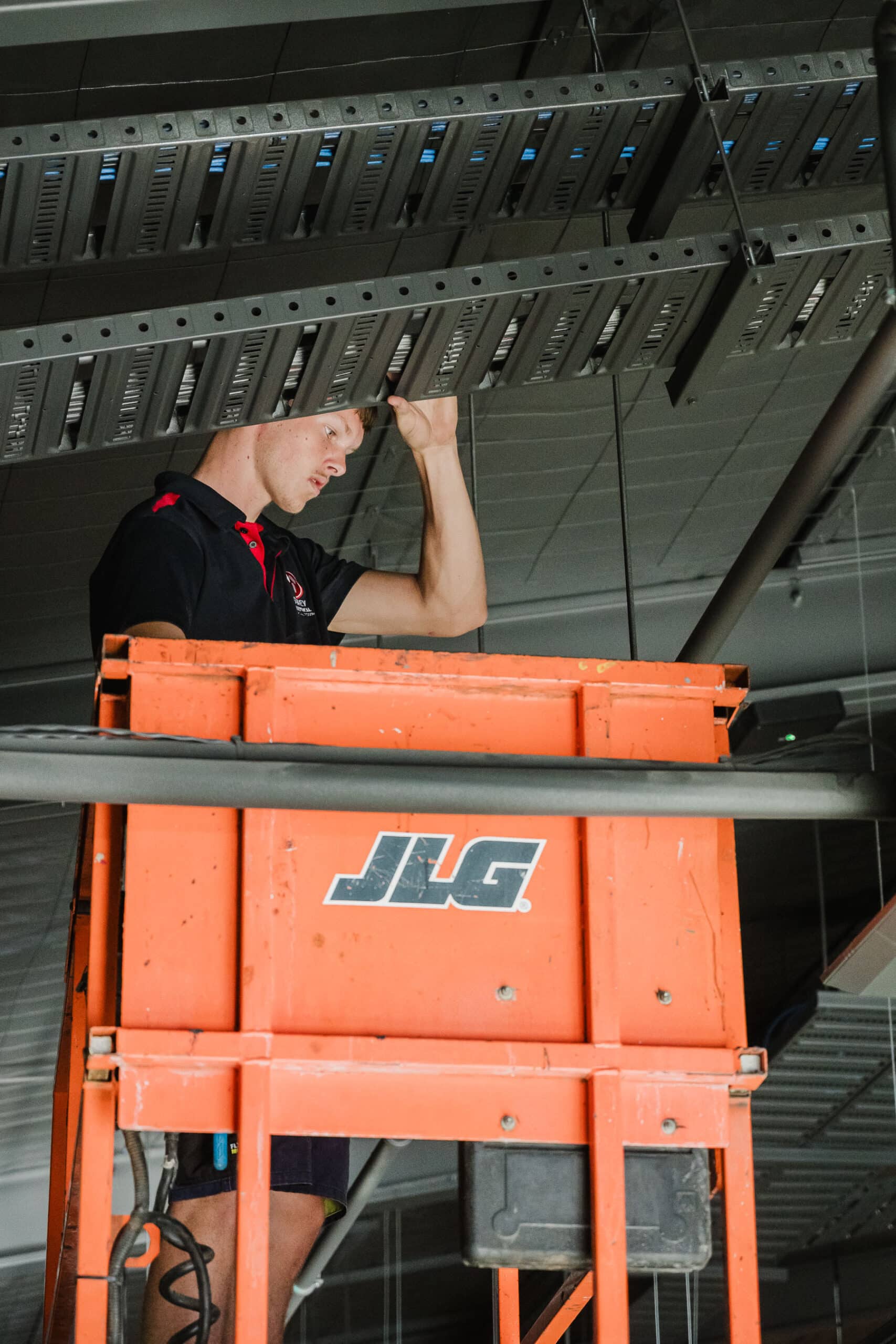 Electrician working from a scissor lift to install or inspect overhead cable trays.