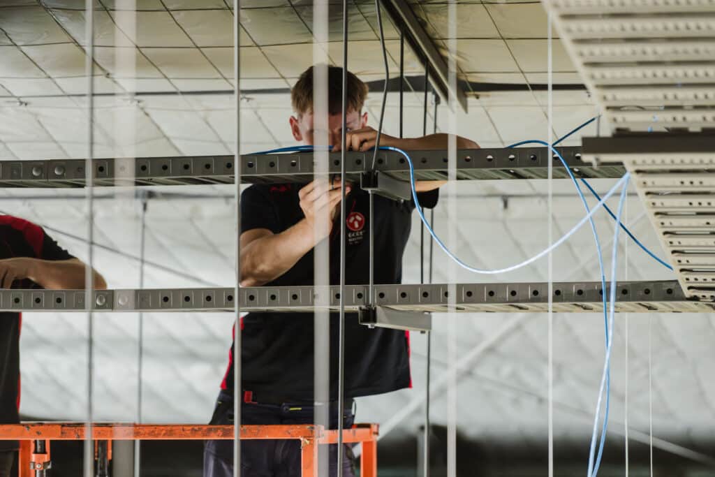 Electrician routing network cables through overhead cable trays in a commercial ceiling.