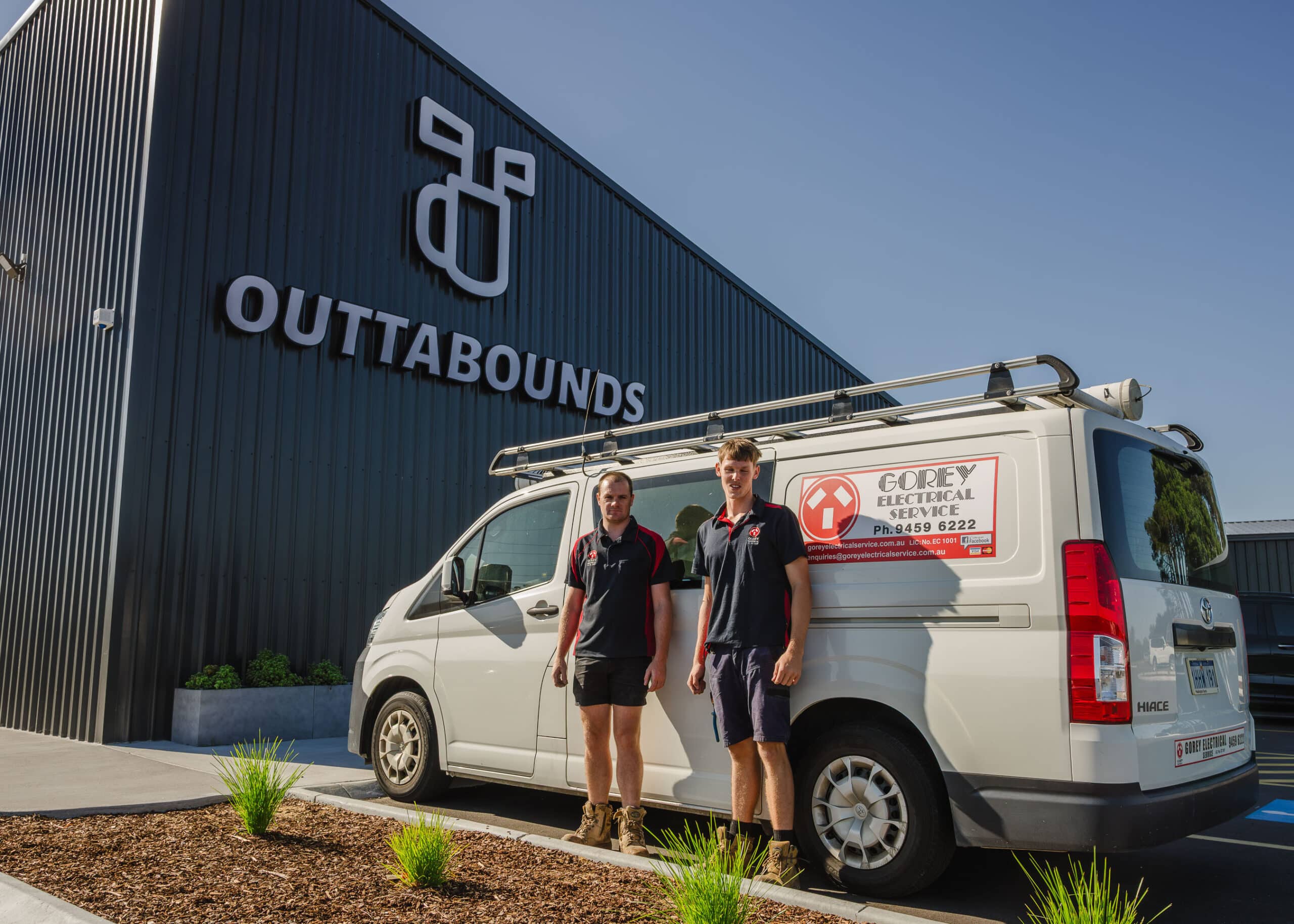 Gorey Electrical Service technicians standing beside a branded service van outside a commercial building.