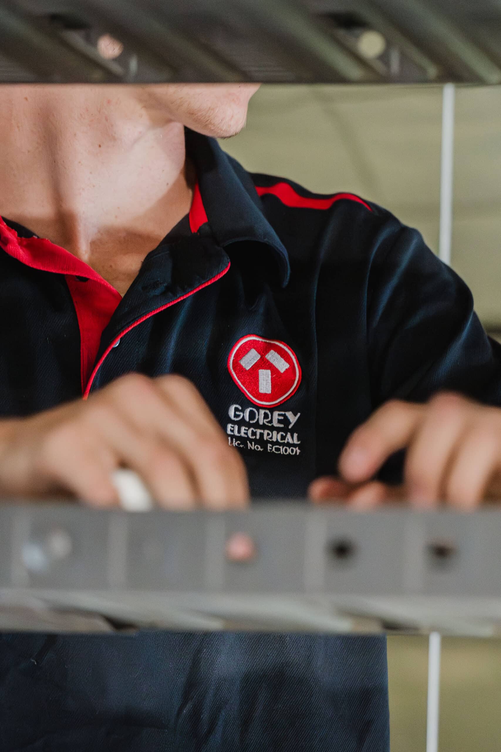 Close-up of a Gorey Electrical Service electrician working on overhead cable tray wiring.